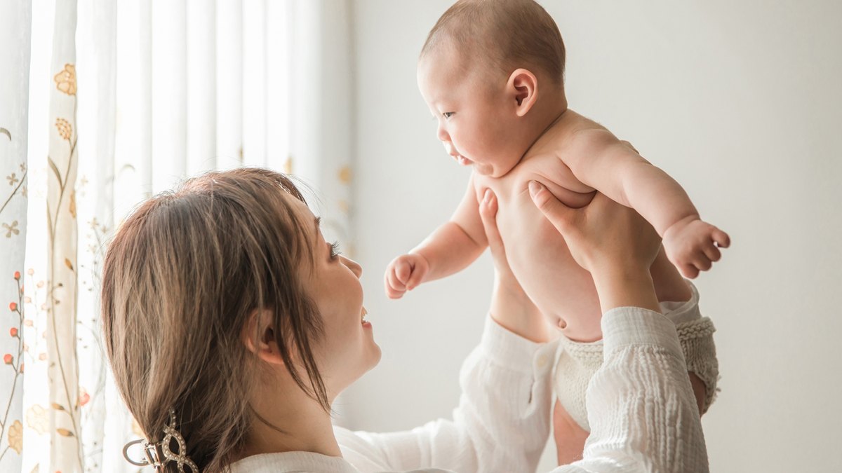 窓辺で赤ちゃんを抱き上げるお母さん